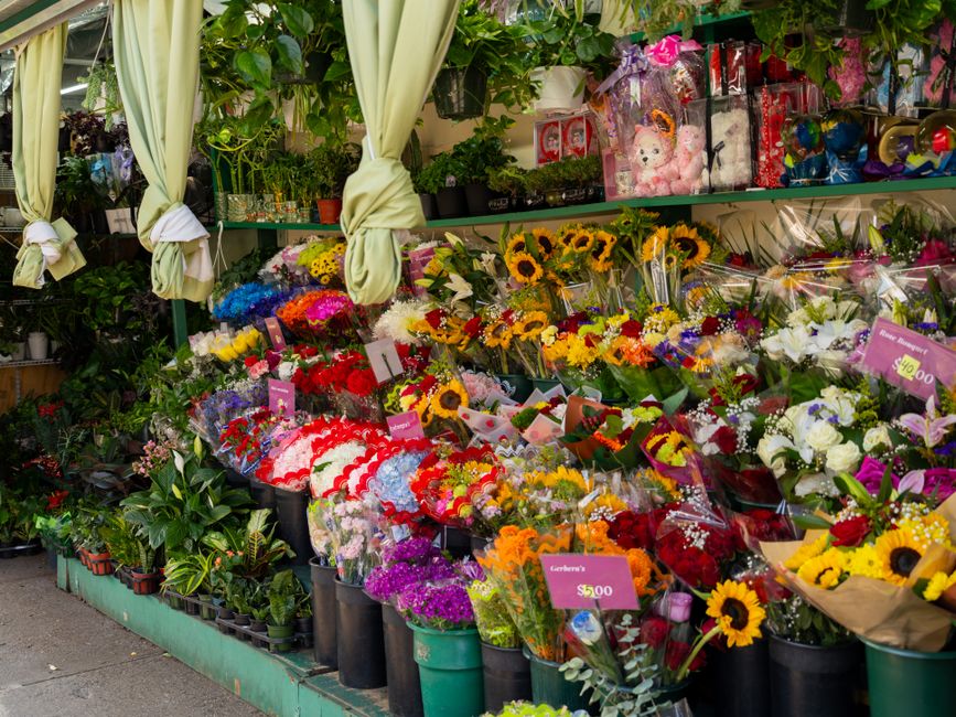 A vibrant display of fresh flower bouquets arranged on a flower shop’s outdoor stand, featuring a variety of colorful blooms including bright yellow sunflowers, white lilies, pink roses, purple chry
