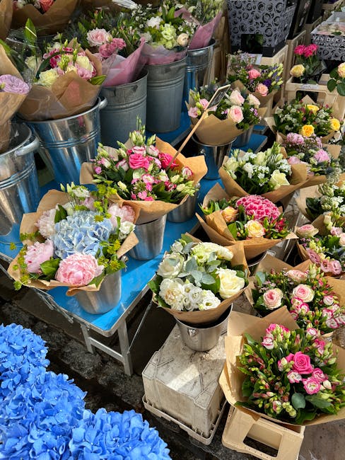 A vibrant display of freshly arranged flower bouquets set on a blue table, featuring a variety of blossoms including pink roses, white lilies, blue hydrangeas, and other colorful flowers wrapped in br